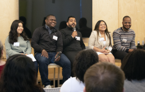 Five panelists sit in front of an audience